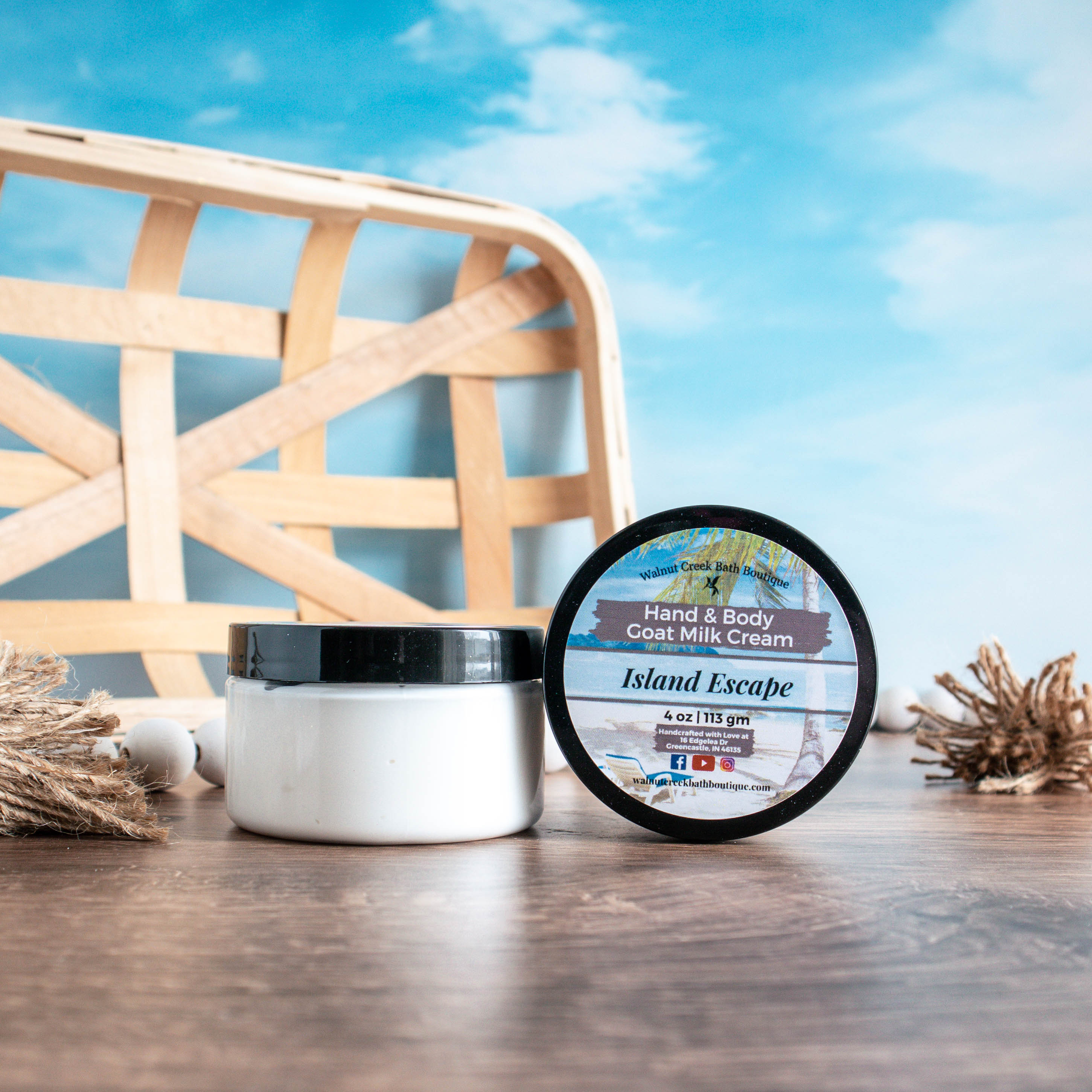a 4 oz jar of island escape cream is sitting to the left of another jar that is on its side so the top is facing outward. There are white wooden beads in the background along with a wood tray. they are sitting on a warm brown board and there is a sky blue background