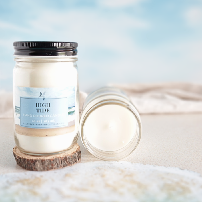 High Tide Candle sitting on a small wood round, with another candle laying on it&
