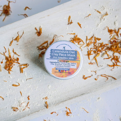 Calendula Oat clay face mask is a small glass jar. This is sitting on a wooden board with calendula petals and clay mask powder surrounding it.