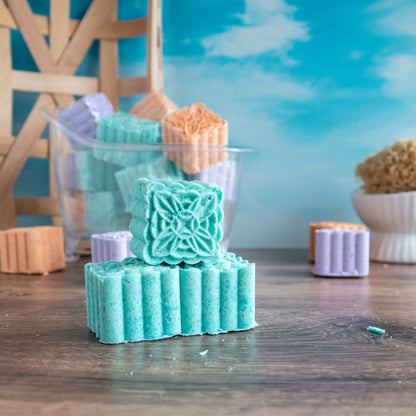 Revive shower steamers stacked. One facing showing a pretty scroll on top of the mint green steamer. There is a mound of steamers in the background. There is a pretty blue sky in the background.